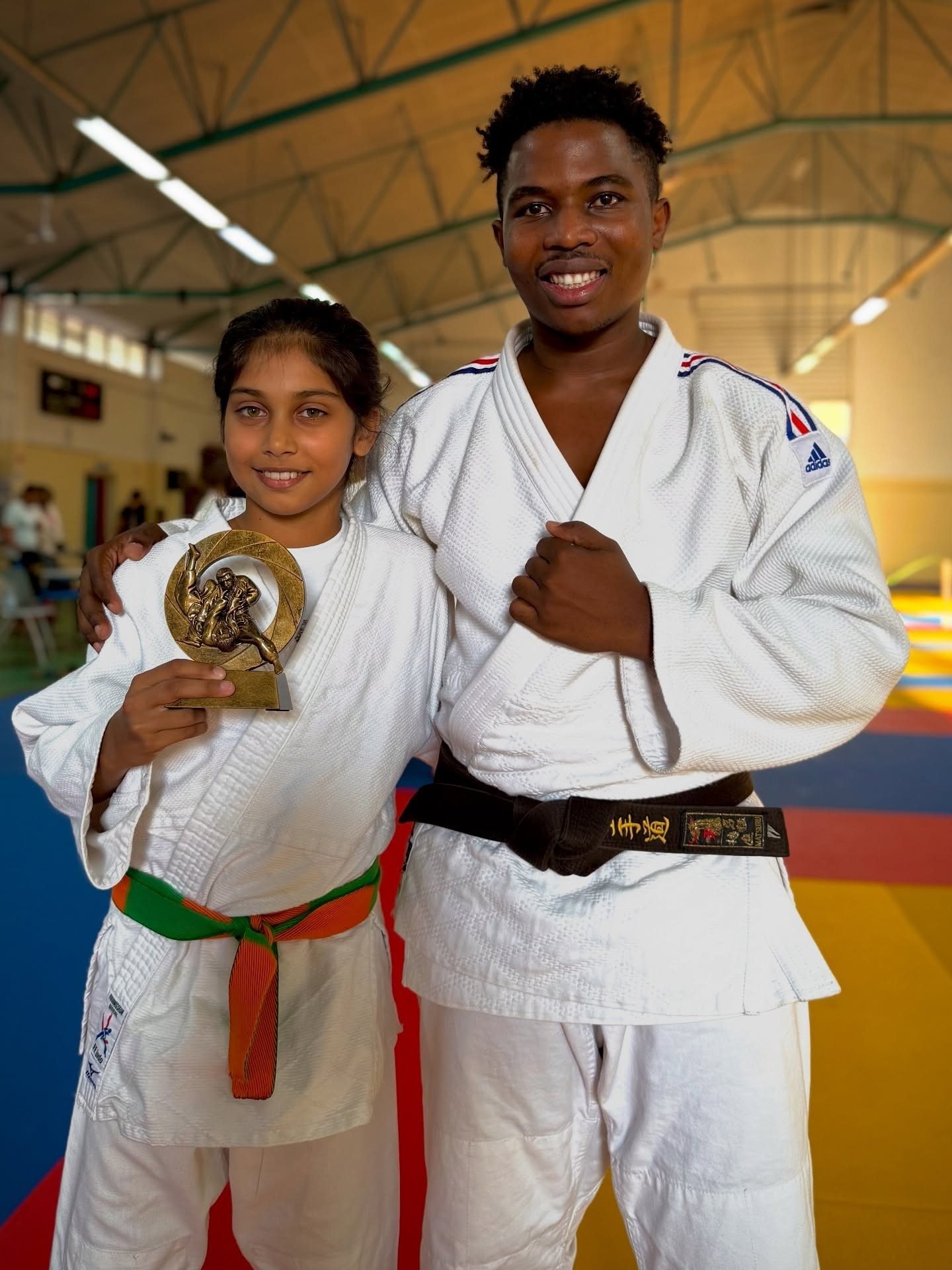 Une jeune judokate présente son trophée aux côtés de son enseignant